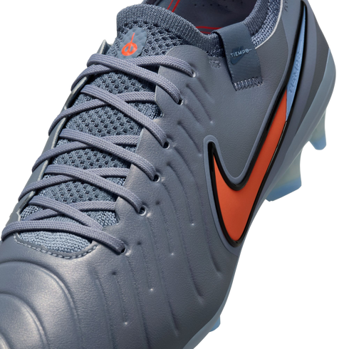 Close-up of a blue-grey Nike Tiempo soccer cleat with a vibrant orange swoosh and matching laces against a black background.