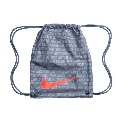 A grey Nike drawstring bag with an orange swoosh. It features a multilingual "Nike soccer" text pattern and grey cords, set against a black background.