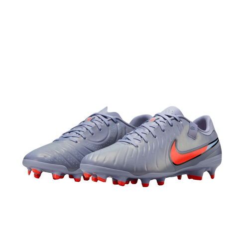 Lavender-grey Nike soccer cleats with a vibrant orange swoosh and orange-tipped studs, shown against a solid black background.