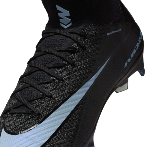 Close-up of a black Nike Mercurial soccer cleat with light blue accents, featuring a textured Gripknit upper, black laces, and an "M" logo on the high-top collar.