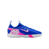 A blue Nike Mercurial turf soccer shoe with white and pink accents, featuring a large "M" logo on the heel, isolated against a black background.