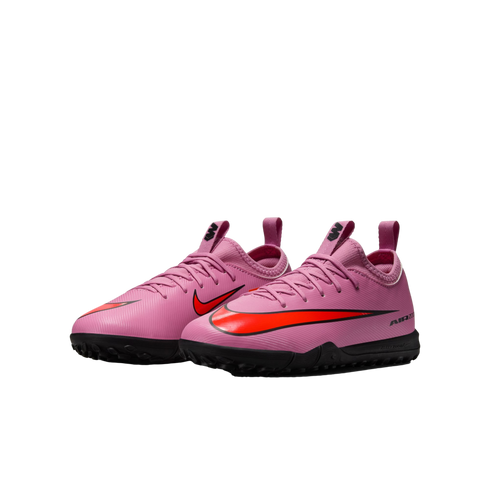 A pair of pink Nike turf soccer shoes with bright orange swooshes and black soles, shown against a black background.