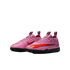 A pair of pink Nike turf soccer shoes with bright orange swooshes and black soles, shown against a black background.