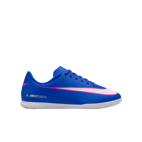 Profile view of a blue Nike Mercurial indoor soccer shoe with a white swoosh outlined in pink and a white sole, set against a solid black background.