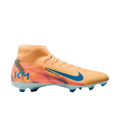 Profile view of a peach and orange Nike soccer cleat with blue accents, featuring a high-top sock collar and a KM logo on the heel.