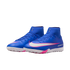 A pair of blue Nike Mercurial turf soccer shoes with a high-top collar, white swoosh outlined in pink, and textured outsoles, displayed against a black background.