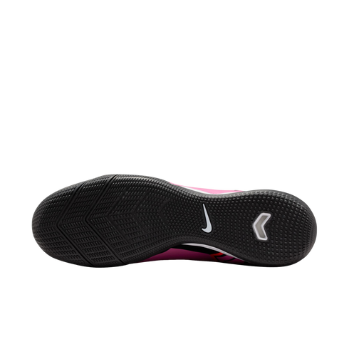 The textured black outsole of a pink Nike indoor soccer shoe, showing the tread pattern, a white Nike swoosh, and a white chevron-shaped logo.