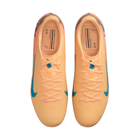 Top-down view of a pair of peach-colored Nike soccer cleats with blue accents and Kylian Mbappé's signature on the insoles.