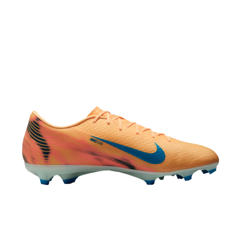 Side profile of a peach Nike soccer cleat with a blue Swoosh and tiger-stripe heel detail. It has a white sole with blue studs, set against a solid black background.