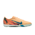 A peach-colored Nike turf soccer shoe featuring a blue swoosh, a graphic heel pattern, and a light green studded outsole.