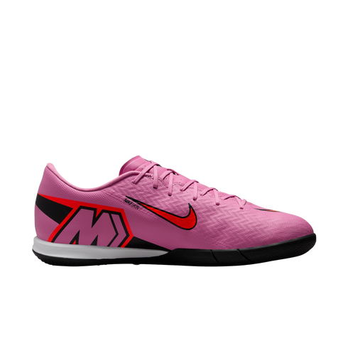 Profile view of a pink Nike indoor soccer shoe with red and black accents and a large "M" logo, isolated on a black background.