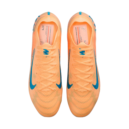 Top-down view of bright orange Nike soccer cleats with blue swoosh accents and Kylian Mbappé "KM" branding on the insoles.