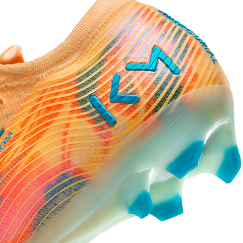 Close-up of an orange and pink soccer cleat featuring blue "KM" branding and blue studs on a translucent sole.