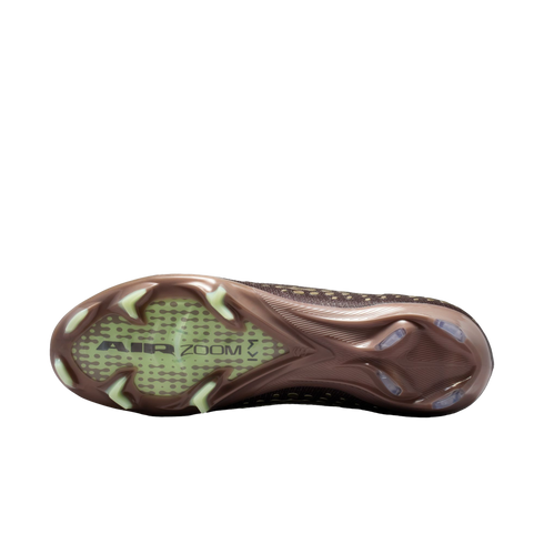 Bottom sole of a bronze Nike soccer cleat with "AIR ZOOM" and "KM" branding, featuring light-colored studs on a solid black background.