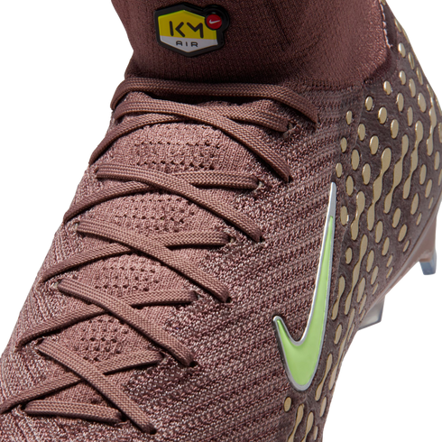 Close-up of a maroon knit Nike soccer cleat featuring a lime green swoosh, gold circular patterns, and a yellow "KM AIR" logo on the high-top ankle collar.