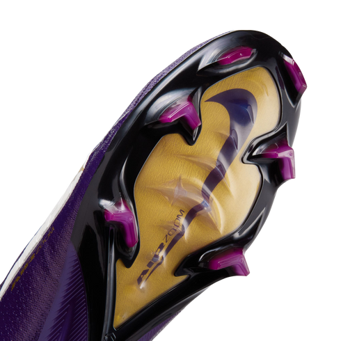 Close-up of a Nike soccer cleat's soleplate featuring a gold and black design, magenta studs, and a large iridescent swoosh over "AIR ZOOM" branding.