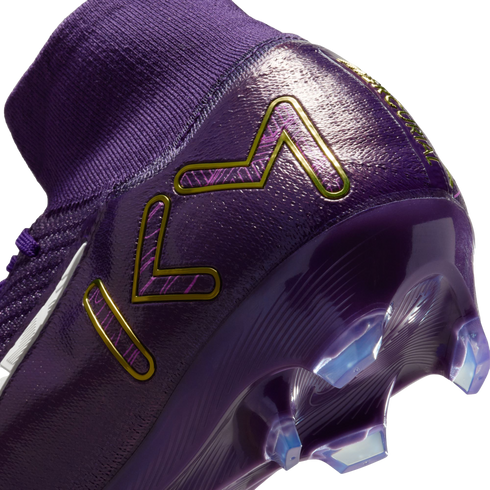 Close-up of a purple Nike Mercurial soccer cleat with a gold KM logo on the heel, featuring a knit ankle collar and clear cleats on the soleplate.