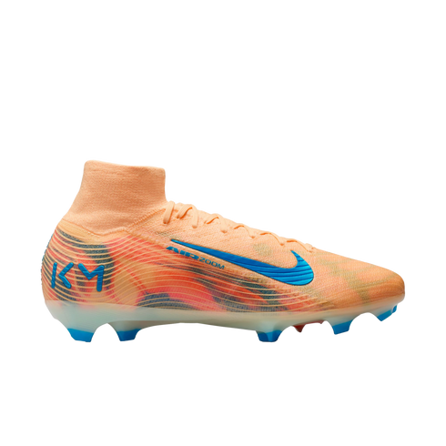 A peach Nike soccer cleat with a colorful graphic pattern, a blue swoosh, and blue "KM" branding on the heel, set against a solid black background.