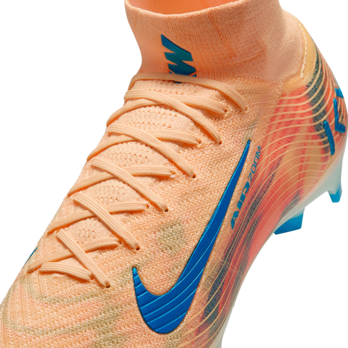 Close-up of a peach Nike soccer cleat featuring a blue swoosh and "AIR ZOOM" branding, with a high-top knit collar and laces against a black background.