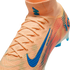 Close-up of a peach Nike soccer cleat featuring a blue swoosh and "AIR ZOOM" branding, with a high-top knit collar and laces against a black background.