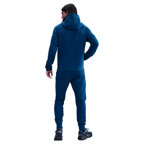 Back view of a person wearing a teal hoodie and matching sweatpants with blue sneakers, against a solid black background.
