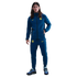 A young man with long hair stands in a blue FC Barcelona Nike tracksuit with yellow logos and blue sneakers against a black background.