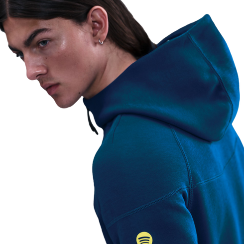 Profile of a person with long hair wearing a dark teal hoodie with a yellow Spotify logo on the sleeve against a black background.