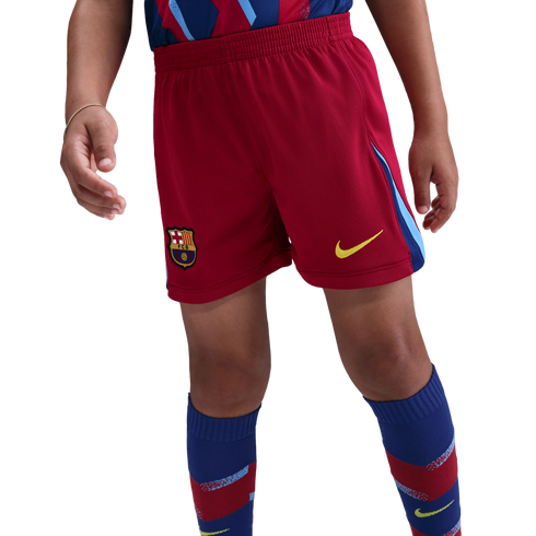 A person wearing red FC Barcelona football shorts with a yellow Nike swoosh and team crest, paired with blue and red patterned knee-high socks.