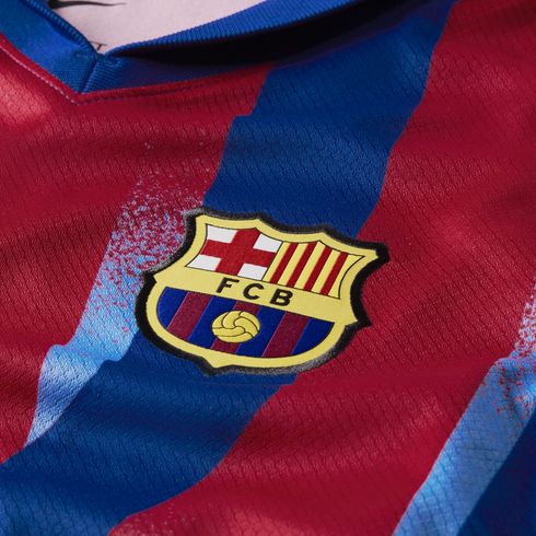 Close-up of an FC Barcelona soccer jersey featuring the embroidered club crest over red and blue vertical stripes.