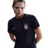 Woman wearing a black USA soccer jersey with red and blue pinstripes and four stars above the crest, posing against a white background.
