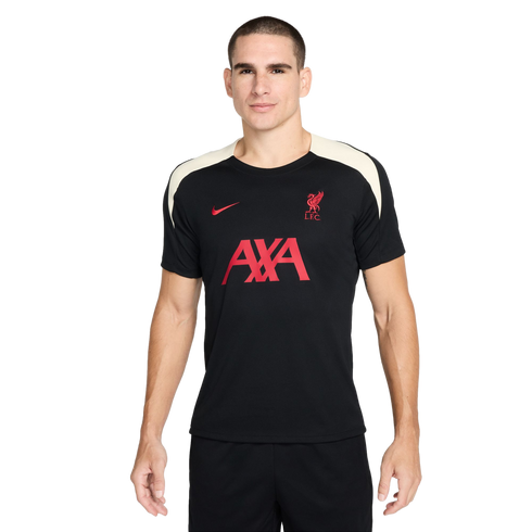 A man stands against a white background wearing a black Liverpool F.C. Nike training shirt with red logos and white shoulder panels.