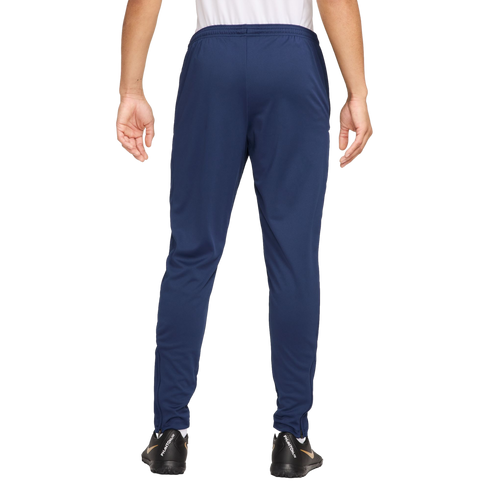 Rear view of a person wearing navy blue track pants and black soccer shoes against a plain white background.