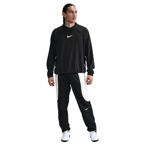 A person wearing a black Nike long-sleeved sweatshirt and black and white track pants with white athletic shoes, standing against a white background.