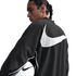 Man with a braid in a black Nike jacket with a large white swoosh on the back, holding a soccer ball. White background.