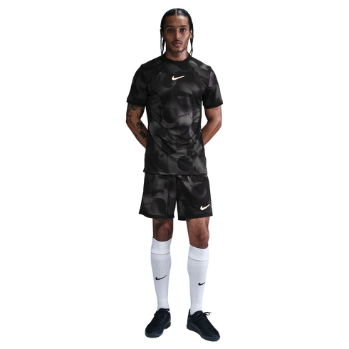 Man in a black patterned Nike soccer uniform with white knee-high socks and black shoes, standing against a plain white background.