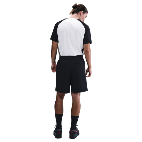 Rear view of a man wearing a black and white raglan T-shirt, black athletic shorts, and black sneakers, standing against a white background.