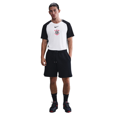 A man wearing a Nike Sport Club Corinthians Paulista t-shirt, black athletic shorts, black crew socks, and black sneakers, standing against a white background.