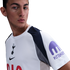 A man wearing a white Tottenham Hotspur jersey with the Kraken logo on the sleeve, looking to the side against a white background.