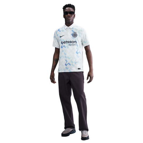 A man wearing a white and blue patterned Inter Milan soccer jersey, dark pants, and sunglasses, standing against a white background.