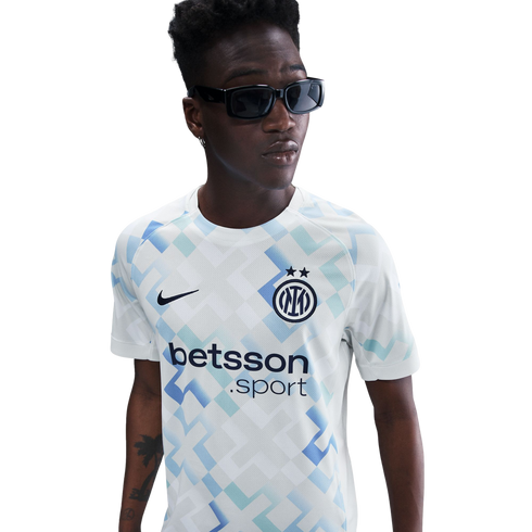 A young Black man in sunglasses wears an Inter Milan football jersey with a blue and teal geometric pattern, set against a solid white background.