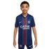 A young boy models a blue Paris Saint-Germain soccer jersey with a red central stripe and matching shorts against a white background. The kit features the club crest and Nike logo.