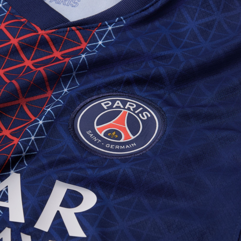 Close-up of a blue Paris Saint-Germain soccer jersey featuring the embroidered team crest, red and white geometric patterns, and partial white sponsor lettering.