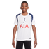A smiling boy wears a white and navy Tottenham Hotspur soccer jersey with the red AIA logo and black shorts, standing against a white background.