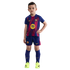 A young boy poses in a full FC Barcelona soccer kit with neon yellow cleats against a black background.