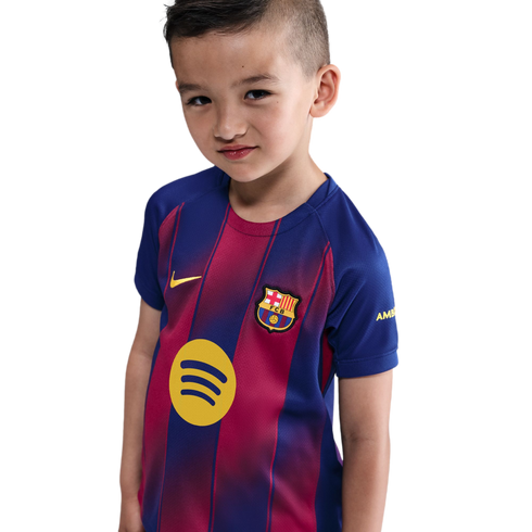 A young boy wearing an FC Barcelona soccer jersey with the Spotify logo, set against a black background.