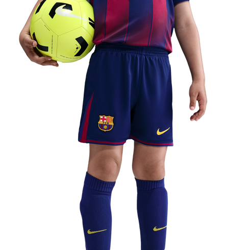 A child wearing an FC Barcelona soccer uniform holds a neon yellow soccer ball against a black background.