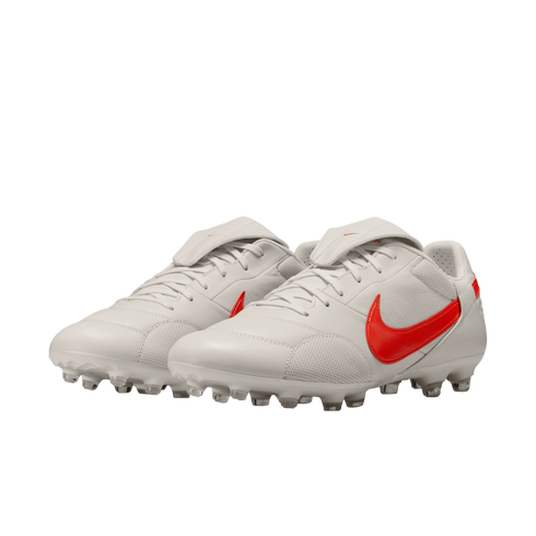 A pair of white Nike soccer cleats with bright red swoosh logos and fold-over tongues on a black background.