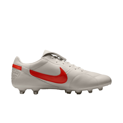 White Nike soccer cleat with a red swoosh against a black background. Features include a perforated leather upper and clear studs.
