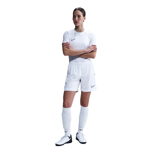 A woman in an all-white Nike soccer kit stands with her arms crossed against a plain white background.
