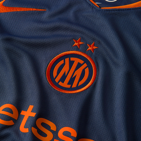 Close-up of a navy blue Inter Milan jersey featuring an orange embroidered crest with two stars, a Nike swoosh, and partial Betsson sponsor logo.